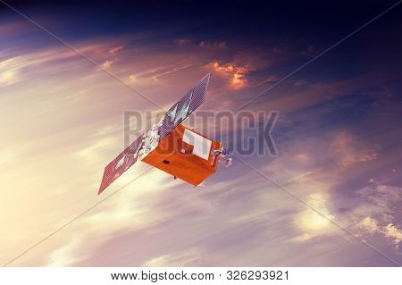 Space Satellite Flying In Orbit Over Sunset Clouds Orbiting Earth. Bright Light From The Sun And Gla