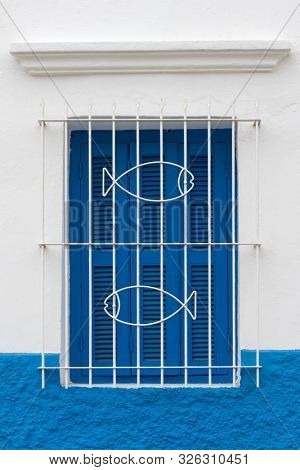 Traditional Moroccan window protected with blue shutters and metal railing decorated with fishes in Asilah, Morocco