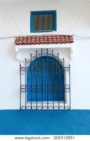  Traditional Moroccan window protected with blue shutters and metal railing in Asilah, Morocco