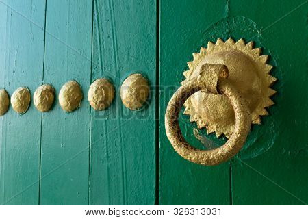 Gold painted doorknocker on a green wooden door in Asilah, Morocco