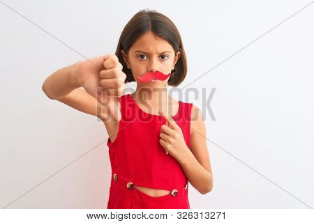 Beautiful child girl holding fanny party mustache standing over isolated white background with angry face, negative sign showing dislike with thumbs down, rejection concept