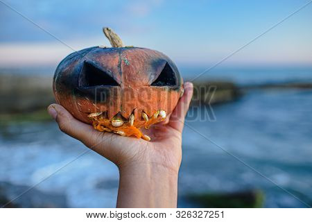Orange Pumpkin Head For Halloween In Hand. A Ghastly Burnt Fire Head Jack