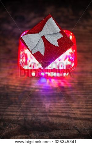 Christmas Present Box With Bow And Glitters Inside Shopping Basket With Colorful Festive Fairy Light