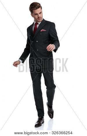 fashion modern businessman wearing double breasted suit and red tie, walking and looking to side, isolated on white background in studio