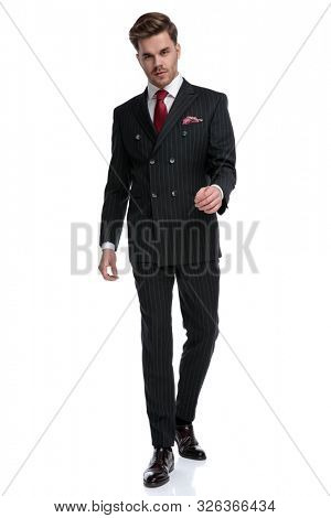 elegant young businessman wearing double breasted suit and red tie, holding hands and walking, isolated on white background 