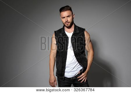 Determined casual man posing and wearing a black jeans vest while standing on gray studio background