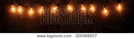 Row of lit string light bulbs glowing on dark grungy background.