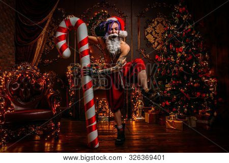 Bad Santa concept. Portrait of a nude tattooed Santa with purple dreads demonstrating antisocial behavior, rudeness and aggression. 