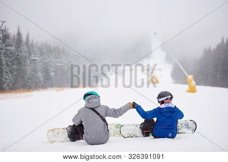 Back View Of Sportsmen Couple Sitting On Snow Before Freeriding From Ski Run At Ski Resort. Man And 