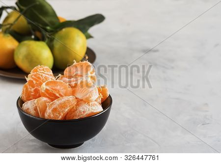 Peeled Fresh Clementine Or Tangerines In A Round Black Bowl, On A Light Background. In The Backgroun
