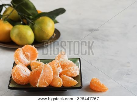 Peeled Fresh Clementine Or Tangerines In A Plate, On A Light Background. In The Background A Group O