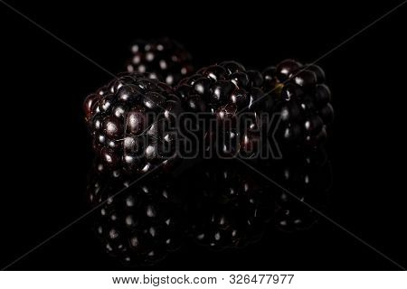 Group Of Four Whole Fresh Black Blackberry Isolated On Black Glass