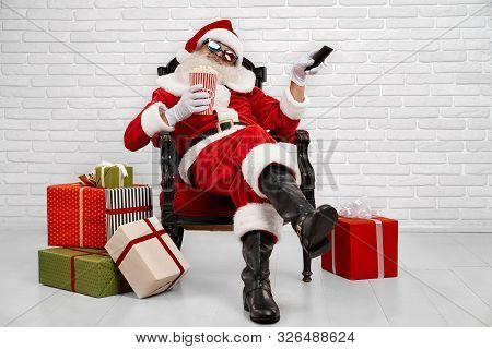 Cheerful Santa Claus In Traditional Costume, White Gloves And 3d Glasses Sitting Comfortably In Armc