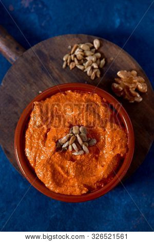 high angle view of a brown earthenware bowl with a homemade muhammara, made with red peppers and walnuts, topped with some fried and salted sunflower seeds, on a table