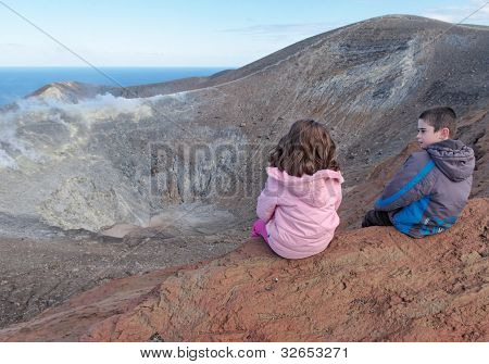 Girl and boy sitting on the rim of volcano crater of Vulcano island near Sicily Italy