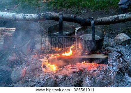 Two Metal Pots Over A Fire. Cooking Dinner At The Stake On The Campfire.