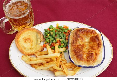 En pub grub stil måltid af en kød pie serveret med blandet grønt, chips, Yorkshire budding og et glas af l