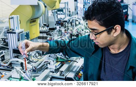 A Young Malay Engineering Student With Spectacles Working In The Lab Repairing And Troubleshooting A