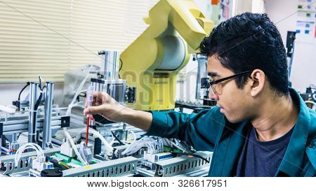 A Young Malay Engineering Student With Spectacles Working In The Lab Repairing And Troubleshooting A