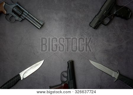 Firearms Laid Out Along The Line. Three Guns Pistols, Army Knives Close-up On A Gray Concrete Backgr