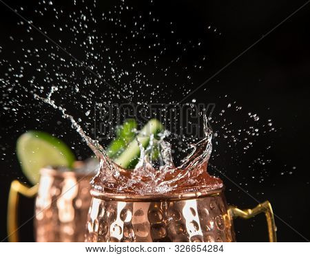 Famous splashing Moscow mule alcoholic cocktail in copper mugs, freeze motion effect.