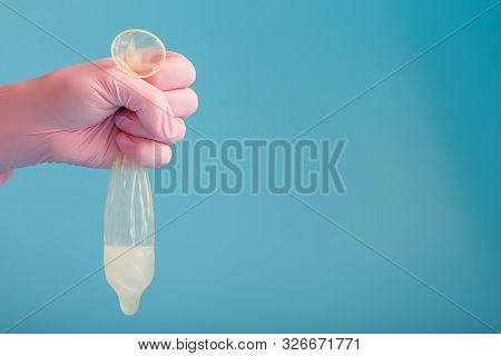 Latex Condom Contraception With Sperm, A Doctor In A Pink Glove Holds A Full Used Condom On A Blue B