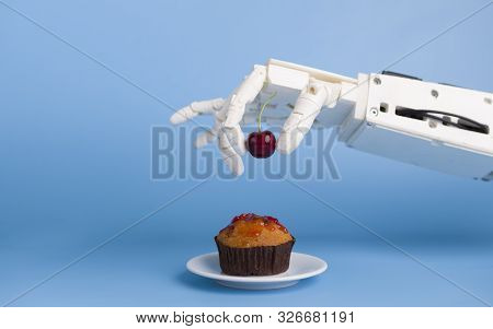 Kitchen Robotization. Robot Hand Putting Fresh Cherry On Top Of The Cupcake, Blue Background