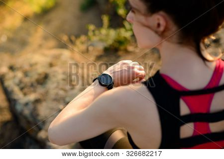 Young Woman Runner Using Multisport Smartwatch at Sunset on the Mountain Trail. Closeup of Hands with Fitness Tracker. Training and Sports Concept.