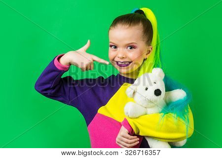 Little Model With Colored Hair Embracing And Pointing On Teddy Bear. The Concept Of Childrens Attach