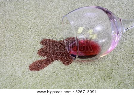 A Glass Of Red Wine Has Been Spilled Onto A White Carpet.