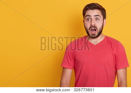 Horizontal Portrait Of Astonished Brunet Man Looks With Surprisment Aside, Wearing Red Casualt Shirt