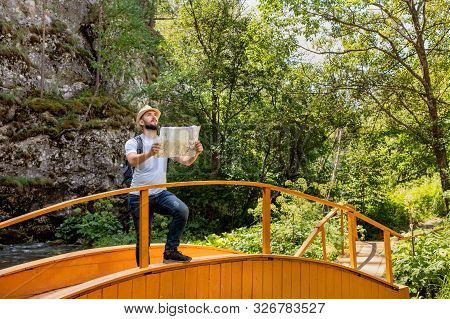 Adventure Man With Map And Backpack On Mountain In Sun Day. Bearded Man Tourist In Mountain Read The