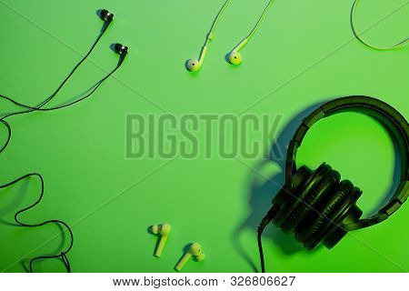 Headphones Of Different Types Flat Lay On Green Color Background, Copy Space. Black In Ear Headphone