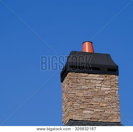 Stone Chimeny With Metal Cap Afainst A Clear Blue Sky