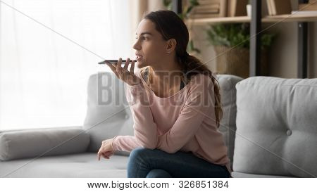 Young Woman Holding Phone Using Mobile Voice Recognition At Home