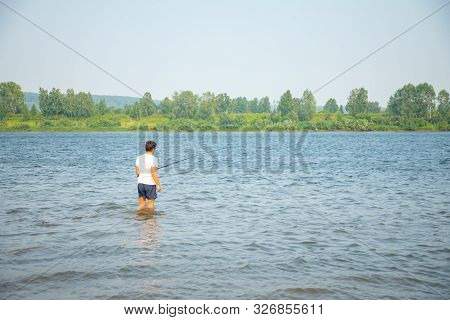A Fisherman Catches Fish Standing In The Water Of River Tom In Kemerovo, Siberia, Russia