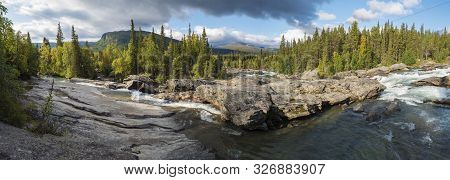 Beautiful Wide Panoramic Landscape With Wild Glacier River Kamajokk, Boulders And Spruce Tree Forest