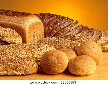 An Assortment Of Breads Sliced And Whole Lying On A Wooden Table And An Orange Background