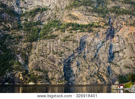 A Lovely Bright Red House Next To A Still Lake With The Reflection Of The Cliff Rock Wall In The Bac