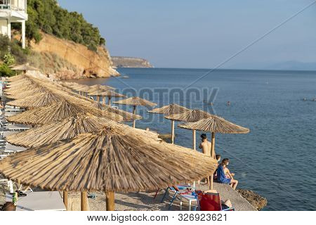 Nafplio Greece - July 19 2019; Sun Shade Umbrellas Lined Up Along Waters Edge In Summer For Beach Go
