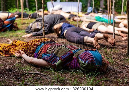 A Colorful And Intergenerational Group Of People Are Seen Laying Face Down In A Muddy Woodland Clear