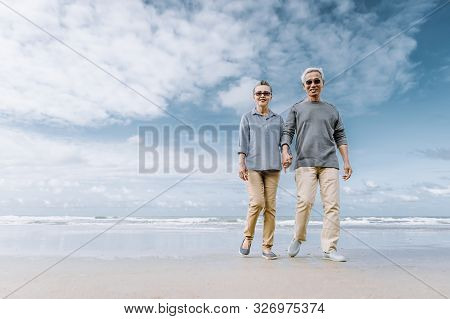 Asian Senior Couple Or Elderly People Walking And Siting At The Beach On Their Weekend Vacation Holi
