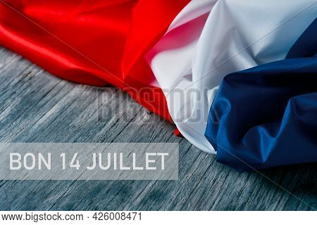 the text bon 14 juillet, happy 14 july, the national day of france written in french, and a french flag on a gray rustic wooden background