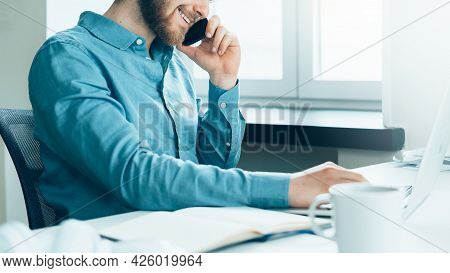 Faceless Smiling Busy Man Entrepreneur In Casual Clothes Talking On Mobile Phone And Looking At Lapt