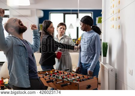 Multi Ethnic Coworkers Play Foosball Game After Work While Drinking Beer Alcohol. Friends Ejnoying S