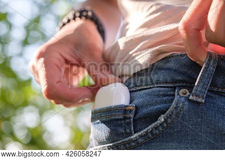 Woman Hand Puts A Case With Wireless Headphones In The Pocket Of Denim Shorts, Outdoors. Close-up.