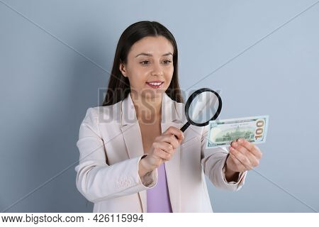 Expert Authenticating 100 Dollar Banknote With Magnifying Glass On Light Grey Background. Fake Money