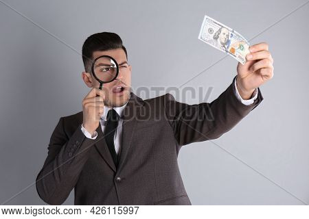 Expert Authenticating 100 Dollar Banknote With Magnifying Glass On Light Grey Background. Fake Money