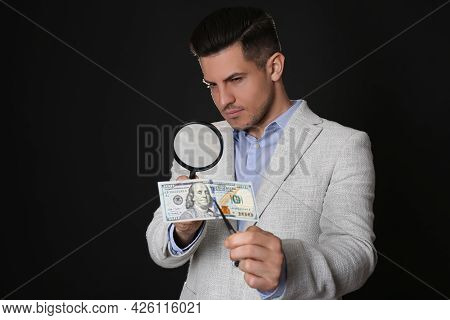 Expert Authenticating 100 Dollar Banknote With Magnifying Glass Against Black Background. Fake Money