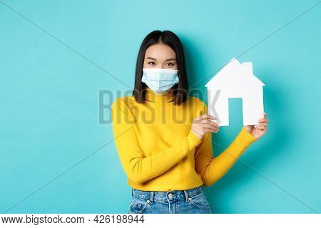 Covid-19, Pandemic And Real Estate Concept. Young Asian Woman In Yellow Clothes Showing Paper House 